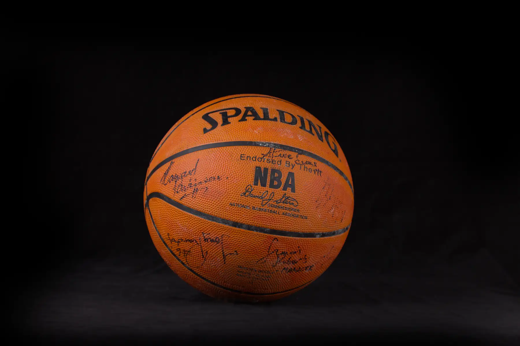 A Spalding NBA basketball signed in black marker across several panels, photographed against black