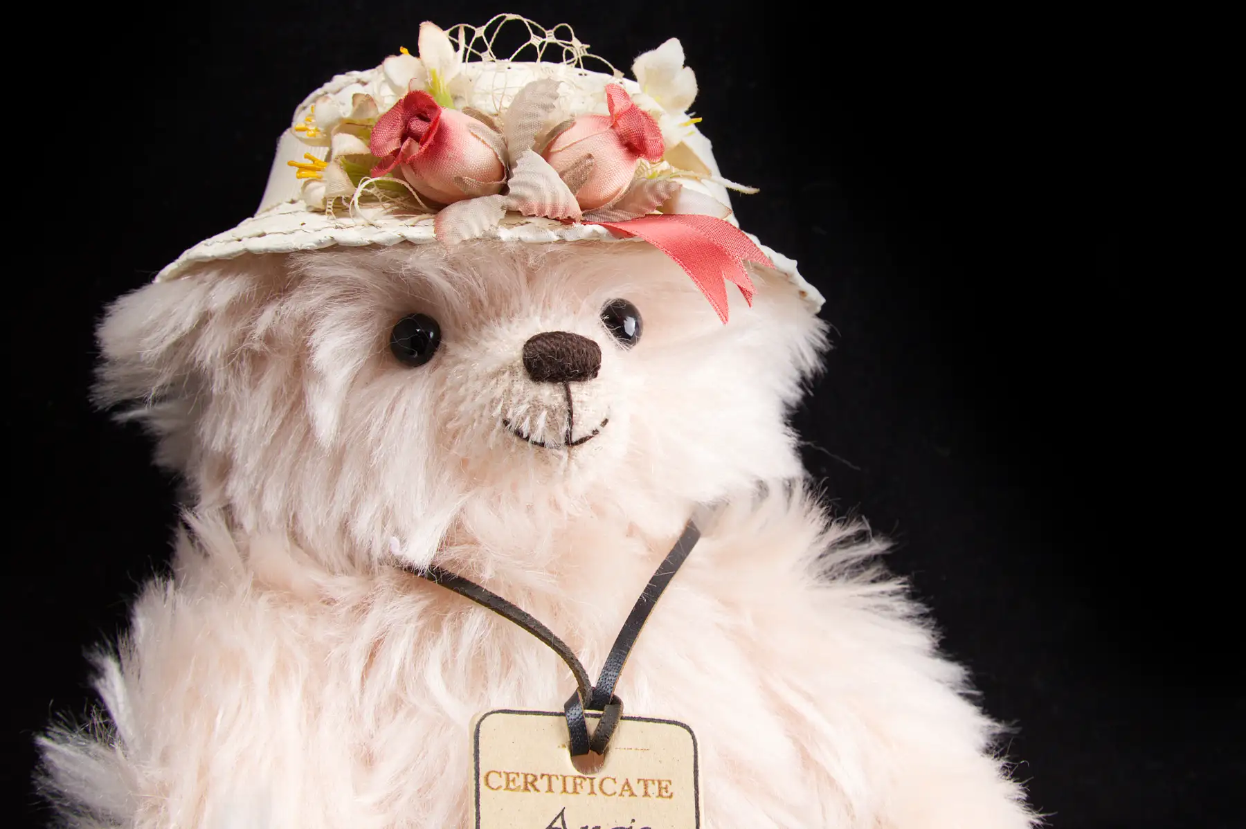 A cream long-pile mohair bear in a straw hat trimmed with pink roses, wearing a swing tag reading Certificate